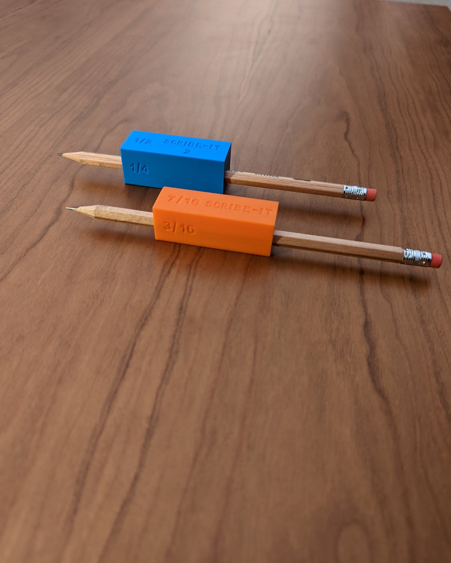 Orange and Blue Scribe-It carpentry scribing tools next to each other with a brown surface in the background.