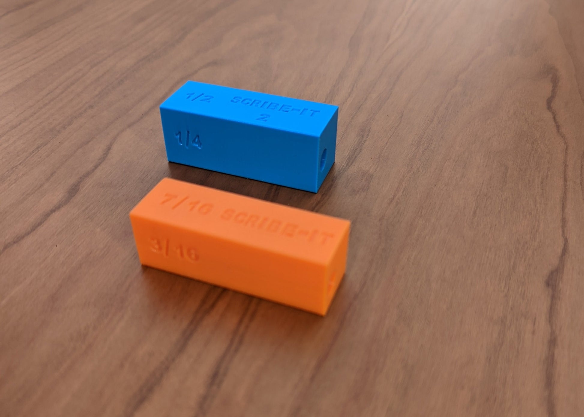Orange and Blue Scribe-It scribing tools next to each other with a brown surface in the background.