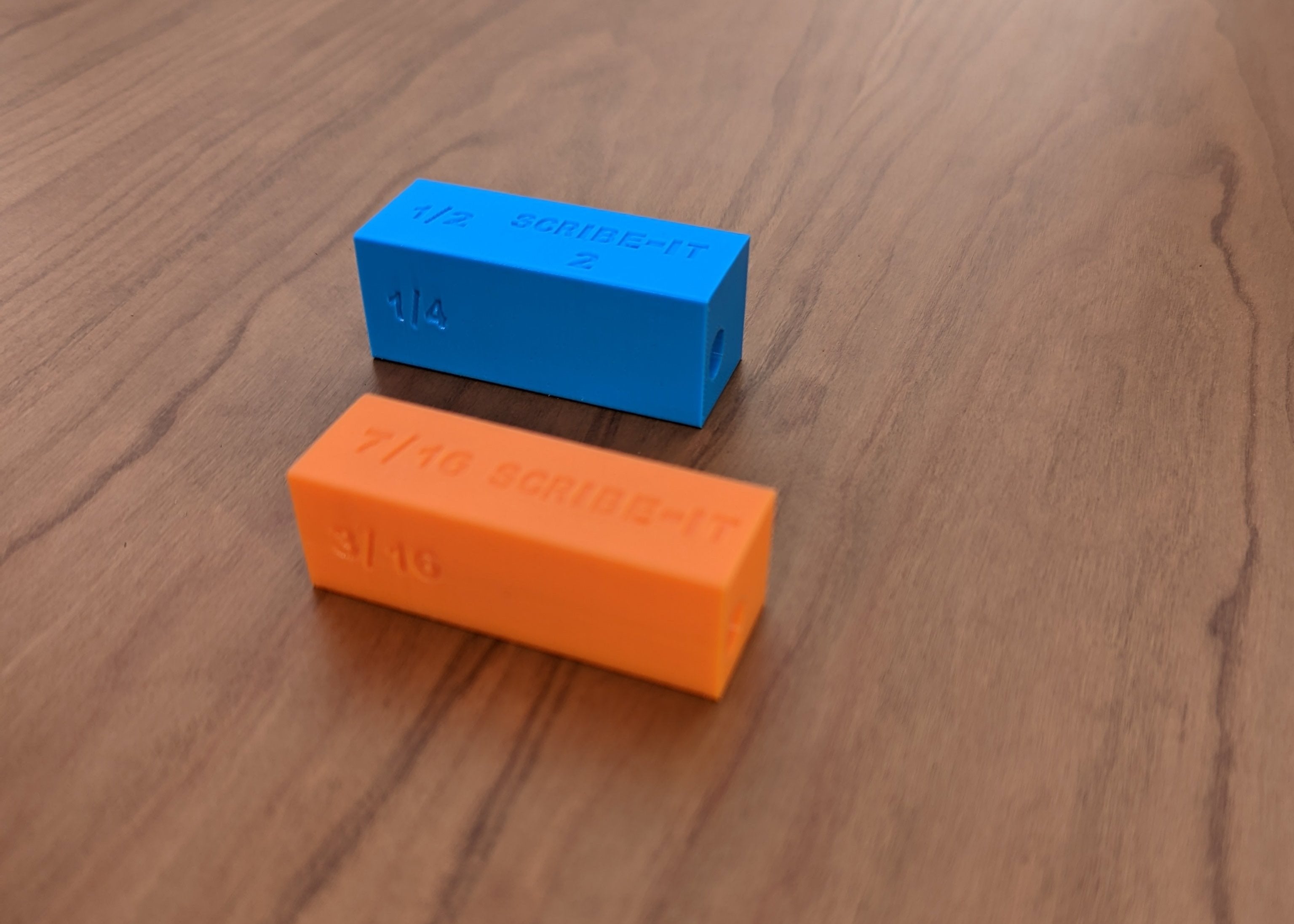 Orange and Blue Scribe-It scribing tools next to each other with a brown surface in the background.